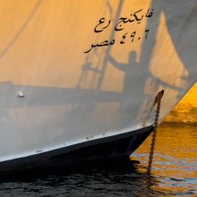 Felucca sailer silhoutted on Nile River cruise boat.